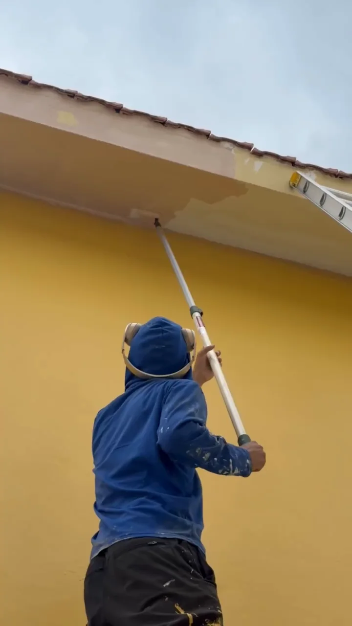 Trabajador pintando el alero de una vivienda con rodillo.